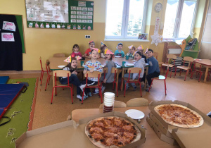 Dzieci uśmiechają się do zdjęcia, na pierwszym planie widać pizzę.