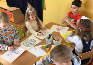 Dzieci siedzą przy stoliku, kolorują i wykonują ćwiczenia na kserówkach.
