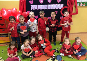 Dzieci ubrane na czerwono pozują do zdjęcia na tle Walentynkowej dekoracji.
