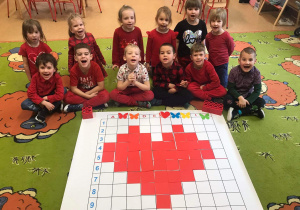 Dzieci siedzą na dywanie i prezentują "zakodowane" serce.