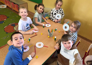 Dzieci siedzą przy stoliku i dekorują donuty z papieru.