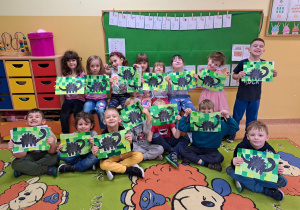 Dzieci pozują do zdjęcia z pracą przedstawiającą dinozaura.