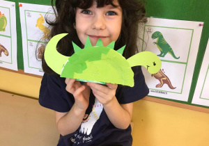 Dziewczynka pozuje do zdjęcia z pracą przedstawiającą dinozaura.