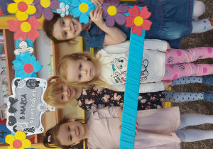 Dziewczynki trzymają ramkę z napisem Dzień Kobiet i uśmiechają się do zdjęcia