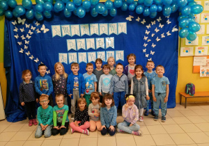 Dzieci ubrane na niebiesko na tle balonów i napisu