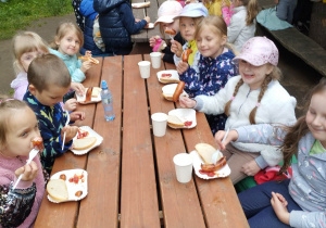 Dzieci jedzą kiełbaski z ogniska.