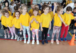 Dziewczynki w żółtych koszulkach stoją ustawione w rzędzie.