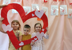 Dwie dziewczynki i chłopiec trzymają serce i pozują do zdjęcia.