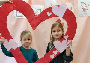 Dwie dziewczynki trzymają serce i pozują do zdjęcia.