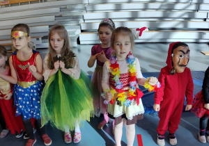 Dziewczynki przebrane w kolorowe stroje tańczą w rytm muzyki.