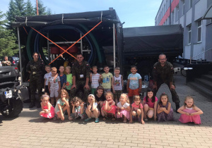 Dzieci wraz z wojskowymi pozują do zdjęcia na tle wojskowego samochodu.