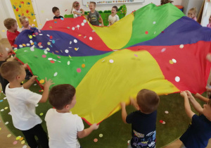 Dzieci podrzucają kolorowe kropki machając chustą animacyjną.