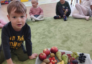 Chłopiec siedzi na dywanie obok niego jest taca z owocami.