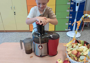 Chłopiec wkłada jabłka do sokowirówki.