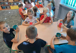Dzieci siedzą przy stolikach i piją soczek jabłkowy, który wcześniej przygotowały.