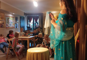 Aktorka w niebieskiej sukni pokazuje dzieciom lalki.