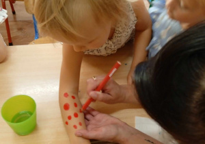 Dziecko ma malowane kropeczki na rączkach.