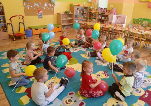 Dzieci siedzą na dywanie i trzymają kolorowe balony