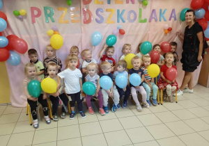 Dzieci pozują do zdjęcia na różowym tle z napisem Dzień Przedszkolaka