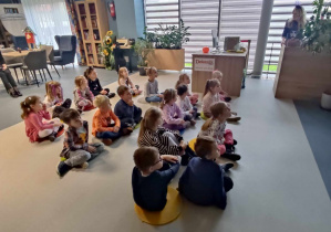 Dzieci siedzą i słuchają bajki czytanej przez panią bibliotekarkę.