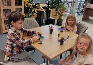 Dzieci siedzą przy stolikach i dekorują nietoperze.
