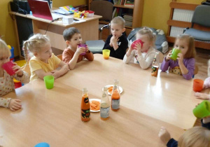 Dzieci siedzą przy stolikach i piją marchewkowe soki