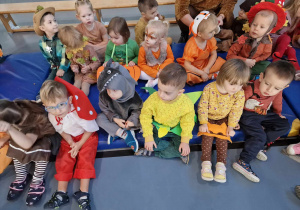 Dzieci przebrane w różne kolorowe stroje siedzą na materacach.