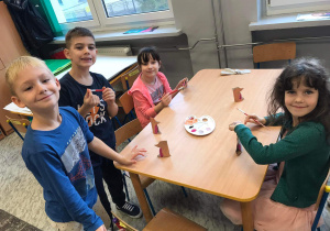 Chłopcy i dziewczynki siedzą przy stoliku i malują farbami.