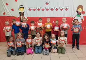 Grupa dzieci z pracą przedstawiającą Polskie Godło pozuje do zdjęcia na tle tematycznej ścianki z okazji Narodowego Święta Niepodległości.