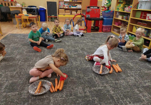 Dziewczynki przekładają marchewki z dywanu do koszyka