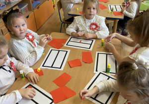 Dziewczynki wyklejają czerwonym papierem szablon flagi Polski.