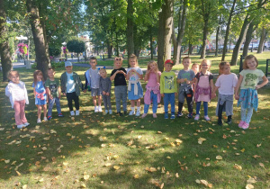 Grupa dzieci stoi na trawniku w parku.