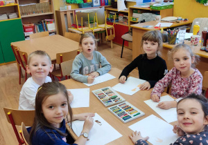 Dzieci pastelami olejnymi na białej kartce malują misia.