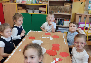 Dzieci siedzą przy stoliku i z papieru wykonują kotyliony.