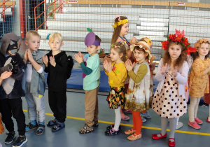 Grupa dzieci przebrane w jesienne stroje klaszcze w ręce.