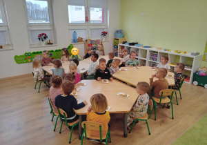 Dzieci siedzą przy stolikach i ozdabiają pierniczki