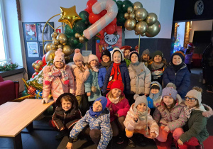 Grupa dzieci pozuje do zdjęcia na tle świątecznej dekoracji z balonów.