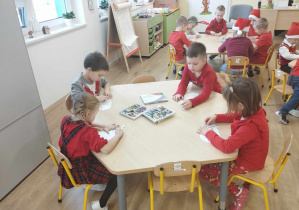Dzieci siedzą przy stoliku i ozdabiają listy do św. Mikołaja.