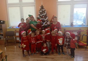 Dzieci ubrane na czerwono w mikołajkowych czapkach pozują do zdjęcia z paniami przebranymi za elfy