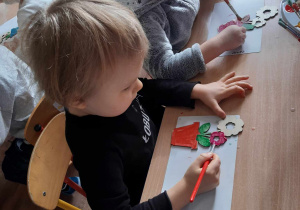 Dziewczynka i chłopiec malują farbami drewniane kwiatki.