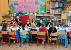 Dzieci siedzą przy stoliku i jedzą słodkie frykasy.