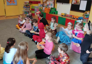Dzieci siedzą na dywanie i klaszczą w ręce w rytm muzyki.