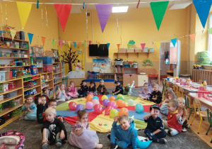 Dzieci siedzą na dywanie przy chuście z balonami