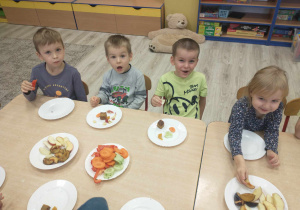 dzieci siedzą przy stole i częstują się owocami