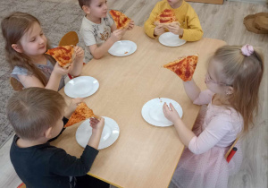 dzieci siedzą przy stole jedząc pizzę