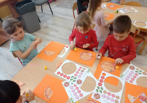 dzieci przyklejają papierowe składniki pizzy do szablonu