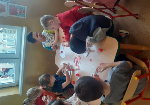 Dzieci wyklejają serduszka czerwonym papierem