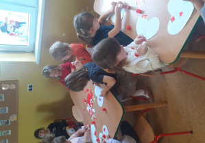 Dzieci wyklejają serduszka czerwonym papierem