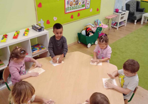 Dzieci siedzą przy stolikach i odbijają rączki w masie solnej