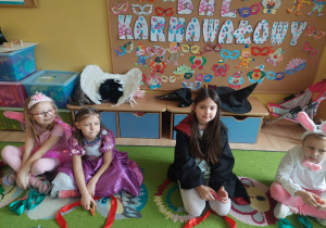 Dzieci przebrane w stroje karnawałowe siedzą na dywanie.